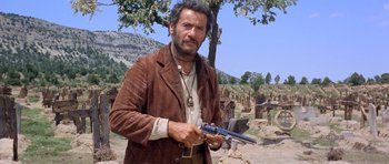 Movie still from “The Good, the Bad and the Ugly” (1966), directed by Sergio Leone – A man holding a gun while standing in a field; Medium shot, Low angle