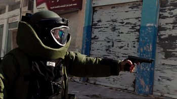 Movie still from “The Hurt Locker” (2008), directed by Kathryn Bigelow – A man in a helmet and a gas mask is holding a gun; Medium shot, Low angle