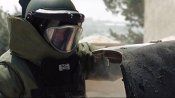 Movie still from “The Hurt Locker” (2008), directed by Kathryn Bigelow – A person in a helmet pointing at something on the side of the road; Close Up shot, Low angle