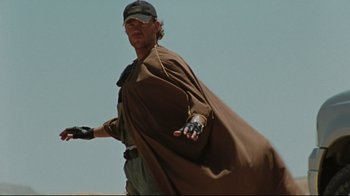 Movie still from “The Hurt Locker” (2008), directed by Kathryn Bigelow – A man wearing a brown cape holding a baseball bat; Medium shot, Low angle