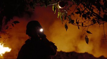 Movie still from “The Hurt Locker” (2008), directed by Kathryn Bigelow – A person with a flashlight is standing in front of a fire; Medium shot, Low angle