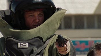 Movie still from “The Hurt Locker” (2008), directed by Kathryn Bigelow – A man wearing a helmet and holding a gun; Close Up shot, Over the shoulder angle