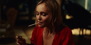 Movie still from “The Idol” (2023), directed by Sam Levinson – A woman in a red shirt is holding a cigarette in her mouth; Close Up shot, Over the shoulder angle
