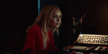 Movie still from “The Idol” (2023), directed by Sam Levinson – A beautiful young lady sitting at a table with a glass of wine; Medium shot, Over the shoulder angle