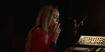 Movie still from “The Idol” (2023), directed by Sam Levinson – A woman sitting at a table with a cigarette in her mouth; Medium shot, Over the shoulder angle