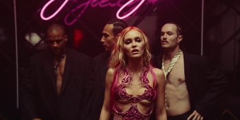 Movie still from “The Idol” (2023), directed by Sam Levinson – A group of men and women standing next to each other in front of a neon sign; Medium shot, Low angle