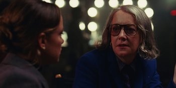 Movie still from “The Idol” (2023), directed by Sam Levinson – A woman in a suit and glasses talking to another woman; Close Up shot, Over the shoulder angle