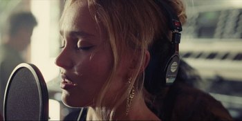 Movie still from “The Idol” (2023), directed by Sam Levinson – A beautiful young lady wearing headphones while posing for a picture; Close Up shot, Low angle