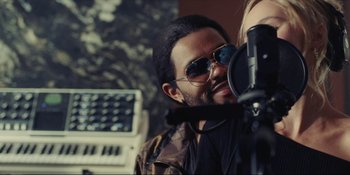 Movie still from “The Idol” (2023), directed by Sam Levinson – A man with a beard and sunglasses is in front of a microphone; Close Up shot, Over the shoulder angle