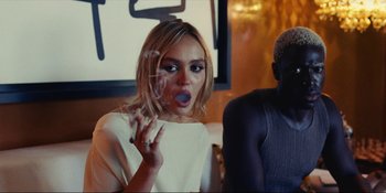 Movie still from “The Idol” (2023), directed by Sam Levinson – A woman smoking a cigarette while holding a cigarette holder; Medium shot, Over the shoulder angle