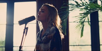 Movie still from “The Idol” (2023), directed by Sam Levinson – A woman standing in front of a microphone in front of a window; Medium shot, Low angle