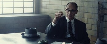 Movie still from “Bridge of Spies” (2015), directed by Steven Spielberg – A man sitting at a table holding a cigarette in his hand; Medium shot, Over the shoulder angle