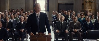 Movie still from “Bridge of Spies” (2015), directed by Steven Spielberg – A man in a suit stands at a podium in front of a group of people; Medium shot, Over the shoulder angle