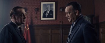 Movie still from “Bridge of Spies” (2015), directed by Steven Spielberg – A man in a suit standing in front of a wall with a picture of an older man; Close Up shot, Over the shoulder angle