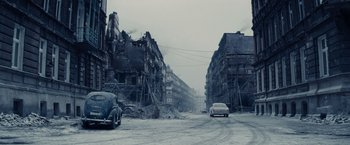 Movie still from “Bridge of Spies” (2015), directed by Steven Spielberg – A car driving down a street next to buildings; Extreme Wide shot, High angle