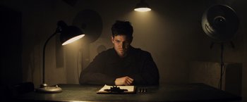 Movie still from “Bridge of Spies” (2015), directed by Steven Spielberg – A man sitting at a table in a dimly - lit room; Medium shot, Low angle