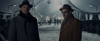 Movie still from “Bridge of Spies” (2015), directed by Steven Spielberg – A man wearing a hat and glasses standing next to another man in a hat; Medium shot, Over the shoulder angle