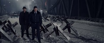 Movie still from “Bridge of Spies” (2015), directed by Steven Spielberg – A man standing in front of a pile of wooden posts; Wide shot, High angle