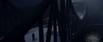 Movie still from “Bridge of Spies” (2015), directed by Steven Spielberg – A person standing in the snow near a bridge; Extreme Wide shot, High angle