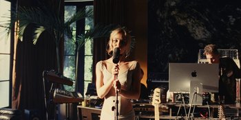 Movie still from “The Idol” (2023), directed by Sam Levinson – A woman holding a microphone in a room; Medium shot, Low angle