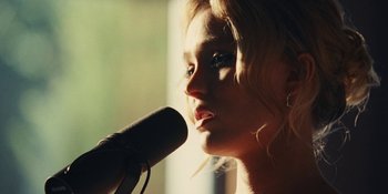 Movie still from “The Idol” (2023), directed by Sam Levinson – A person holding a microphone near a window; Close Up shot, Low angle