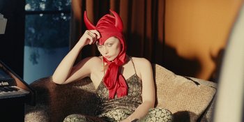 Movie still from “The Idol” (2023), directed by Sam Levinson – A woman sitting on a couch wearing a red hat; Medium shot, High angle