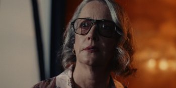 Movie still from “The Idol” (2023), directed by Sam Levinson – An older woman wearing glasses looking at the camera; Close Up shot, Low angle