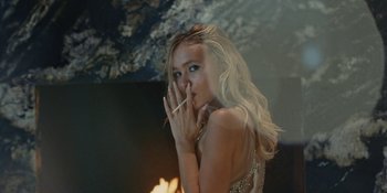 Movie still from “The Idol” (2023), directed by Sam Levinson – A beautiful blond woman holding her hand to her face; Medium shot, Over the shoulder angle