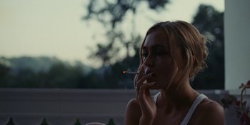 Movie still from “The Idol” (2023), directed by Sam Levinson – A woman is smoking a cigarette in the dark; Close Up shot, Over the shoulder angle