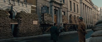 Movie still from “The Imitation Game” (2014), directed by Morten Tyldum – A man riding a bike past a building with a sign on it's side; Extreme Wide shot, High angle