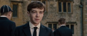 Movie still from “The Imitation Game” (2014), directed by Morten Tyldum – A man in a suit and tie standing in front of a stone building; Close Up shot, Over the shoulder angle