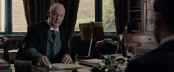 Movie still from “The Imitation Game” (2014), directed by Morten Tyldum – An older man sitting at a table in front of a window; Medium shot, Low angle