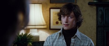 Movie still from “The Last King of Scotland” (2006), directed by Kevin Macdonald – A young man with long hair wearing a brown shirt; Close Up shot, Over the shoulder angle