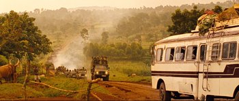 Movie still from “The Last King of Scotland” (2006), directed by Kevin Macdonald – A group of trucks driving down a dirt road near a forest; Extreme Wide shot, High angle