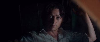Movie still from “The Last King of Scotland” (2006), directed by Kevin Macdonald – A man with long dark hair is looking at the camera; Close Up shot, Over the shoulder angle