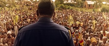 Movie still from “The Last King of Scotland” (2006), directed by Kevin Macdonald – A crowd of people gathered in a field with trees; Extreme Wide shot, Over the shoulder angle