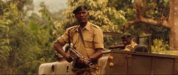 Movie still from “The Last King of Scotland” (2006), directed by Kevin Macdonald – A man in a uniform holding a rifle in front of a car; Medium shot, Low angle