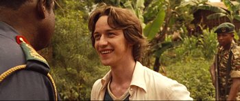 Movie still from “The Last King of Scotland” (2006), directed by Kevin Macdonald – A man with long brown hair smiling for the camera; Close Up shot, Over the shoulder angle