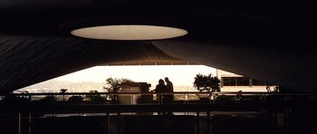 Movie still from “The Last King of Scotland” (2006), directed by Kevin Macdonald – Two people standing under an awning at an airport; Extreme Wide shot, Low angle
