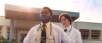 Movie still from “The Last King of Scotland” (2006), directed by Kevin Macdonald – A man with a stethoscope standing next to another man; Medium shot, Low angle
