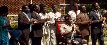 Movie still from “The Last King of Scotland” (2006), directed by Kevin Macdonald – A group of men standing next to each other in front of a building; Medium shot, High angle