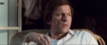 Movie still from “The Last King of Scotland” (2006), directed by Kevin Macdonald – A person sitting on a couch wearing a white shirt; Close Up shot, Low angle