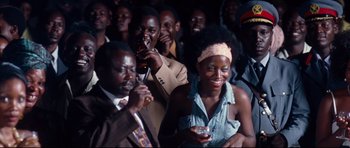 Movie still from “The Last King of Scotland” (2006), directed by Kevin Macdonald – A group of people standing around each other drinking; Medium shot, Over the shoulder angle