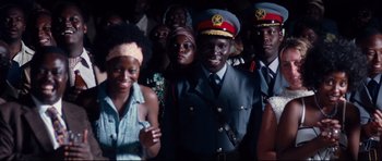 Movie still from “The Last King of Scotland” (2006), directed by Kevin Macdonald – A group of people standing next to each other; Medium shot, Over the shoulder angle