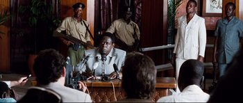 Movie still from “The Last King of Scotland” (2006), directed by Kevin Macdonald – A man sitting in front of microphones in a courtroom; Medium shot, Over the shoulder angle
