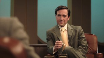 Movie still from “The Last of Us” (2023), created by Neil Druckmann – A man in a suit sitting in front of a mirror holding chopsticks; Medium shot, Over the shoulder angle