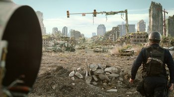 Movie still from “The Last of Us” (2023), created by Neil Druckmann – A man standing in a field with a pile of rubble; Wide shot, Over the shoulder angle