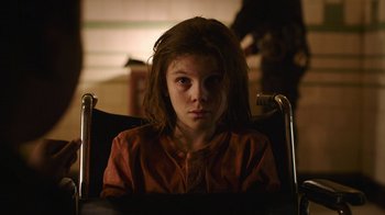 Movie still from “The Last of Us” (2023), created by Neil Druckmann – A young girl sitting in a chair looking into the camera; Close Up shot, High angle