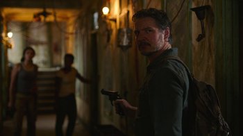 Movie still from “The Last of Us” (2023), created by Neil Druckmann – A man holding a gun while standing next to a wall; Close Up shot, Over the shoulder angle
