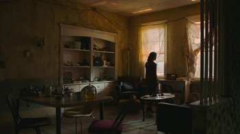 Movie still from “The Last of Us” (2023), created by Neil Druckmann – A woman standing in a room looking out a window; Extreme Wide shot, Low angle